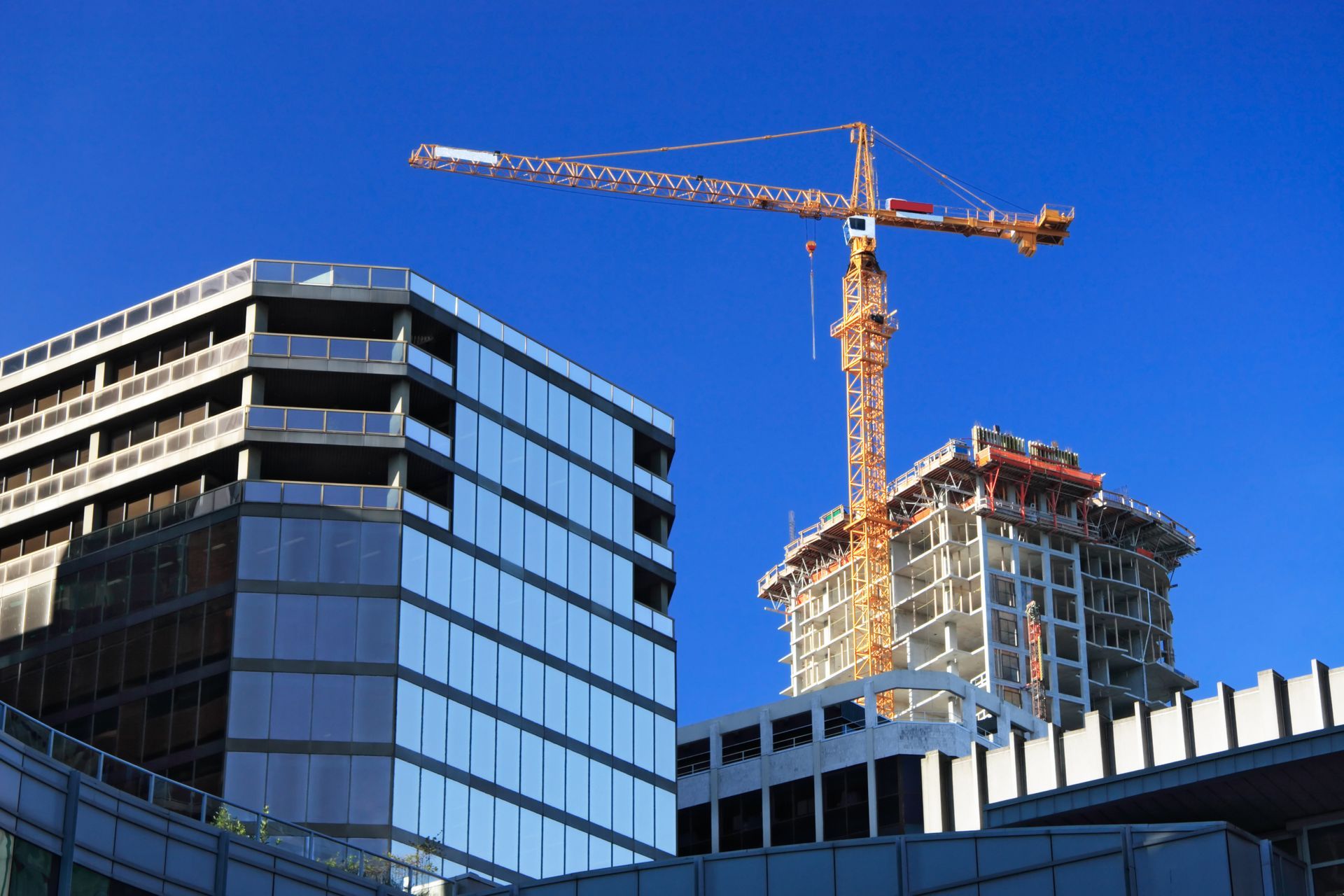 Immeubles de bureaux modernes en verre avec une grue surplombant un chantier de construction, le tout se détachant sur un ciel bleu.