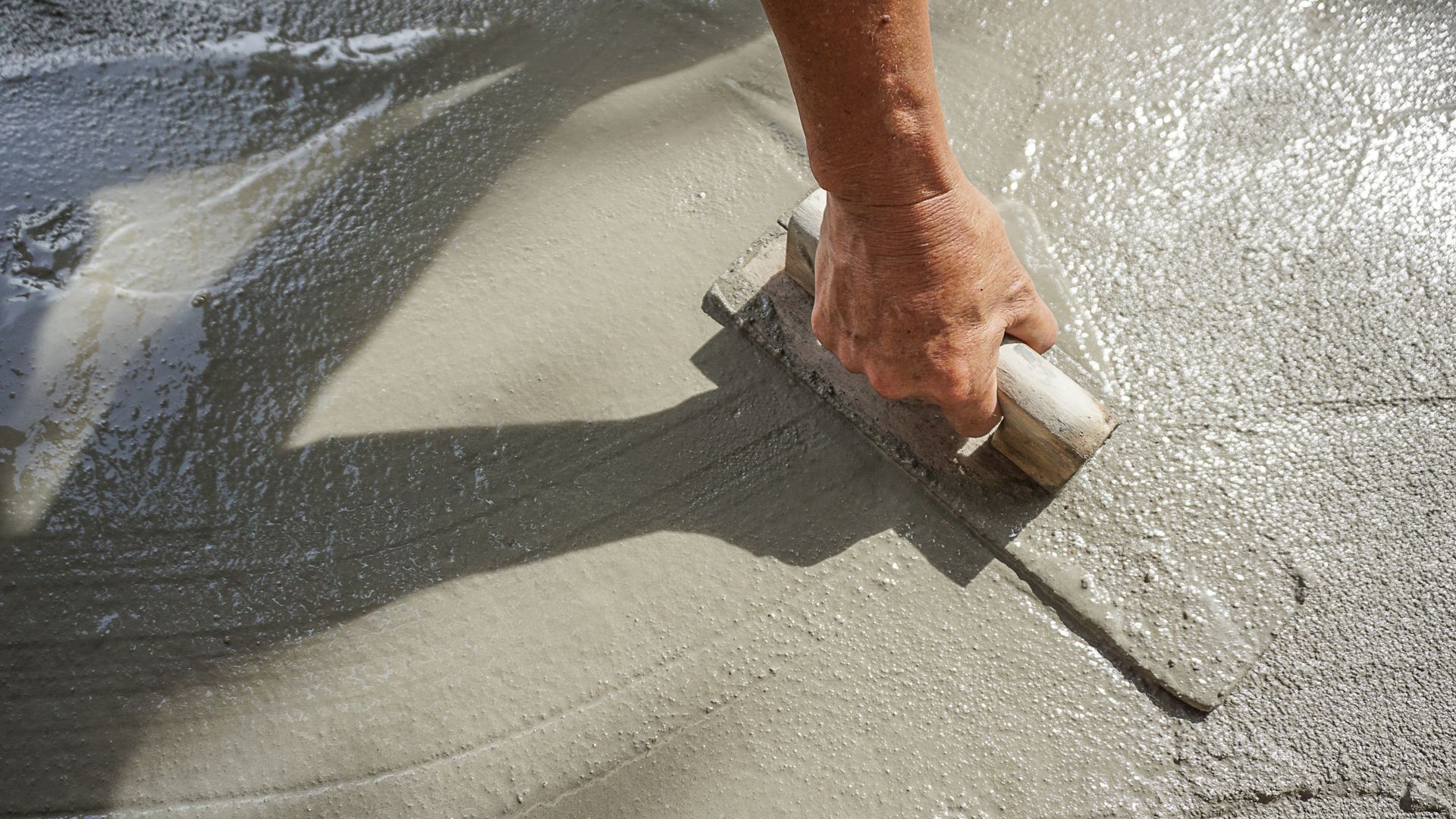 Main appliquant du compos&eacute; de nivellement sur une surface de b&eacute;ton humide avec une truelle.