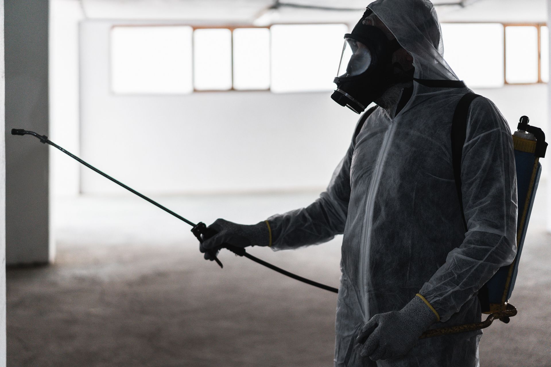 Une personne en combinaison de protection pulvérise du désinfectant dans un entrepôt intérieur.