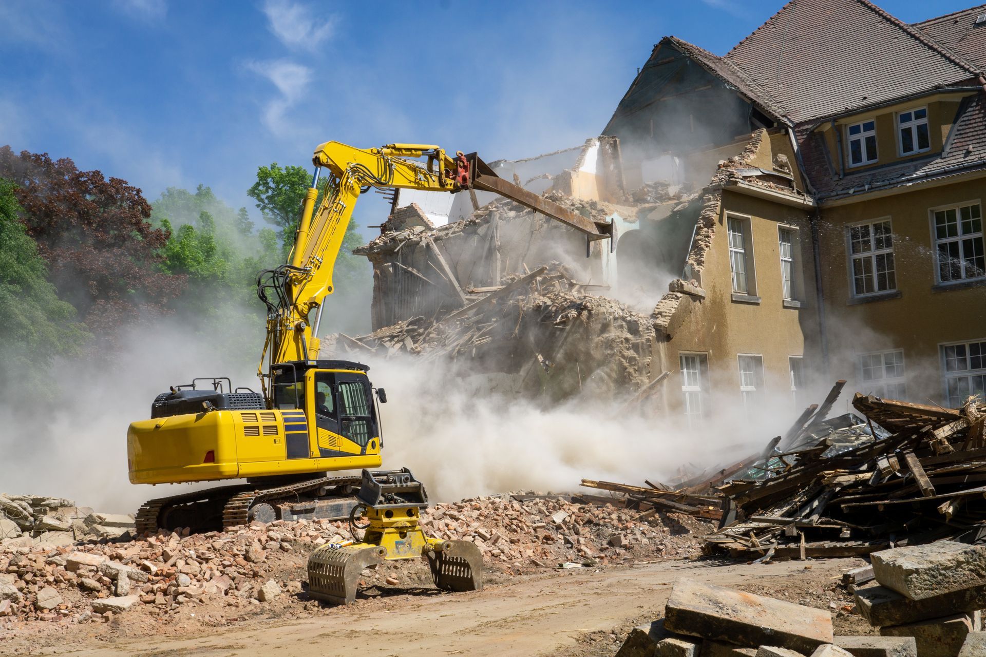 Une pelleteuse jaune démolit un bâtiment au milieu de la poussière et des décombres.