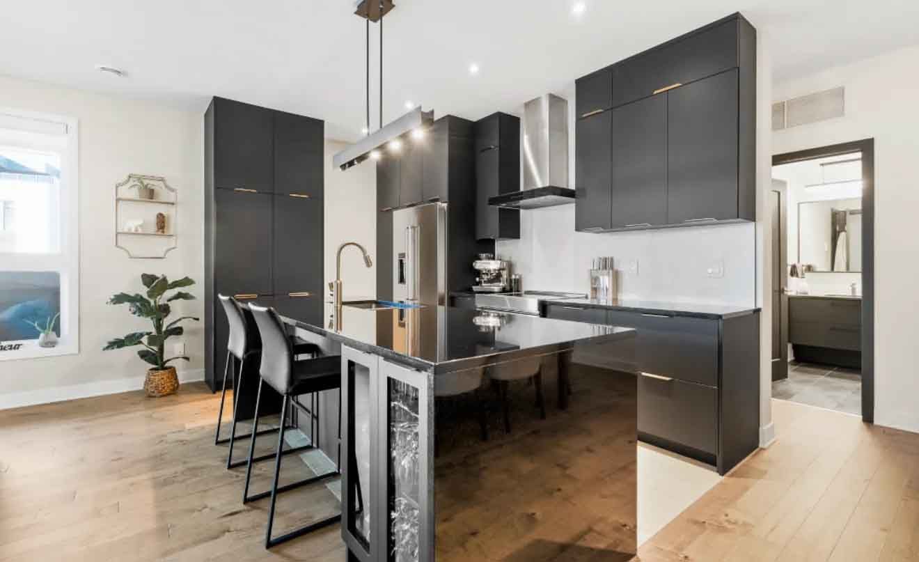 Cuisine moderne avec armoires noires, &icirc;lot central, appareils inox et tabourets de bar.