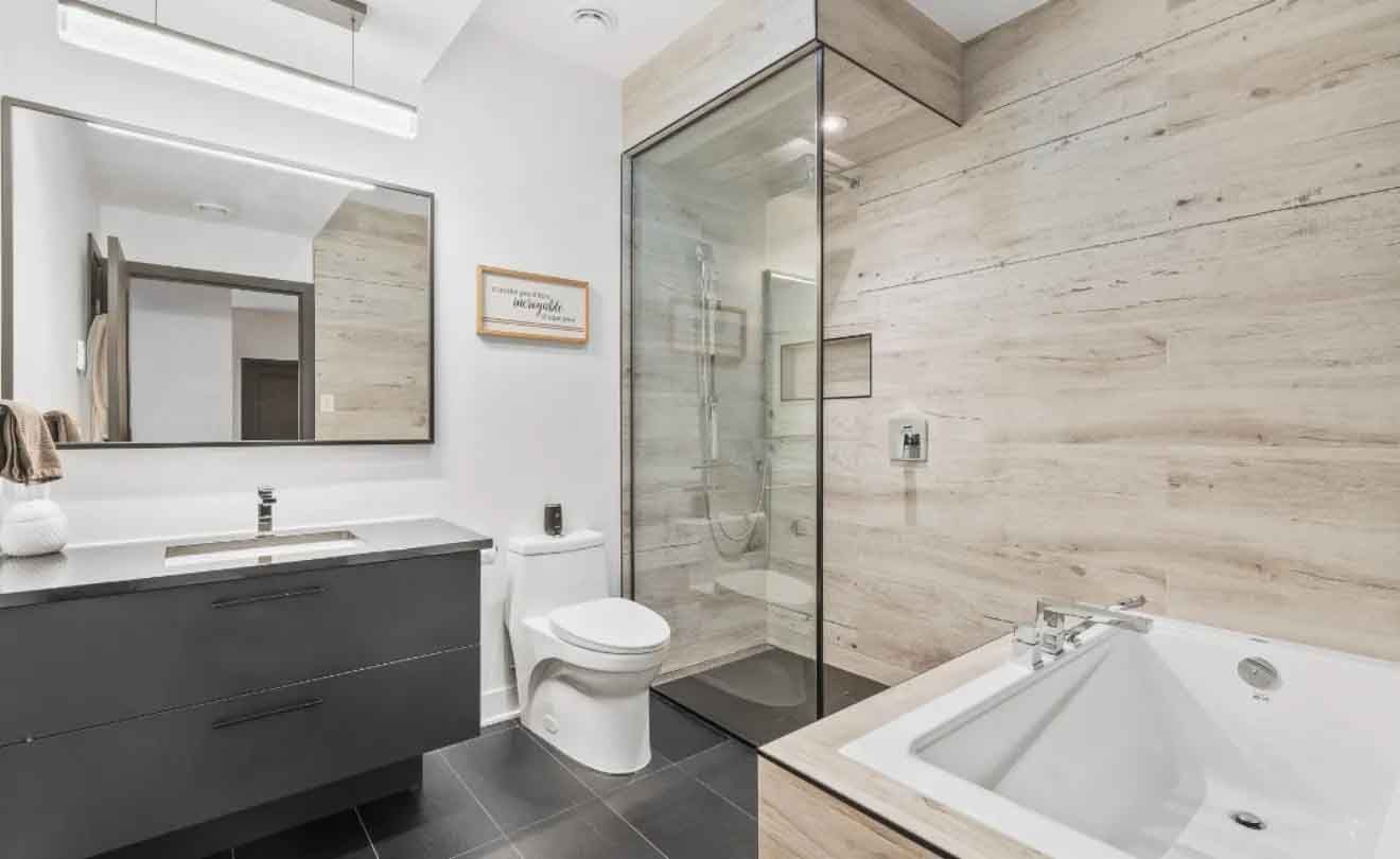 Salle de bains moderne avec douche en verre, baignoire blanche, meuble-lavabo foncé et grand miroir.