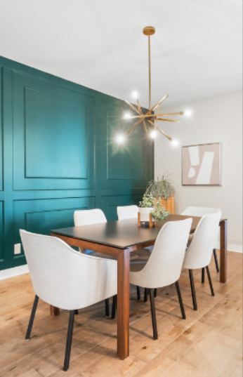 Salle à manger avec un mur d'accent turquoise, une table en bois, des chaises blanches et un lustre doré