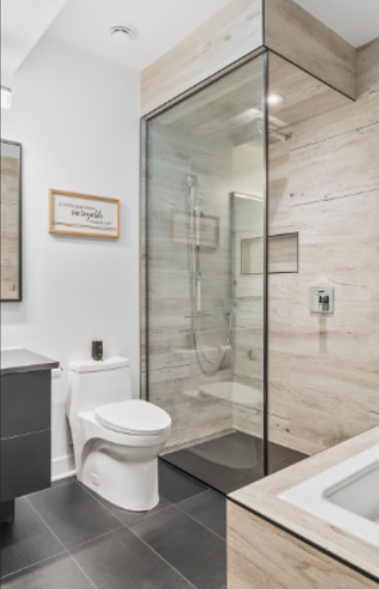 Salle de bains moderne avec douche en verre, toilettes blanches, sol carrelé foncé et murs en bois clair