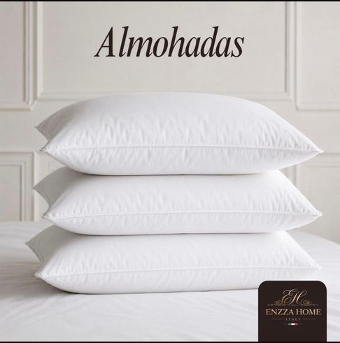 Almohadas blancas y grises cuidadosamente dispuestas sobre una cama beige en un dormitorio con iluminación tenue.