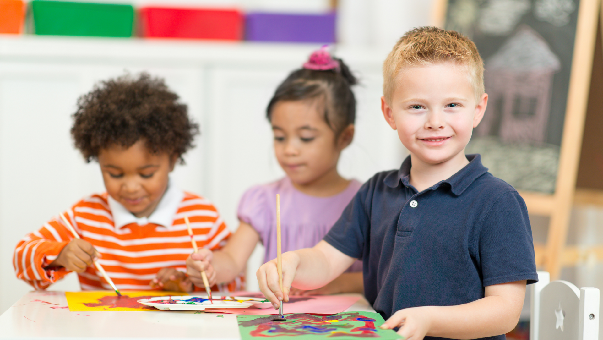 A group of children are sitting at a table painting.