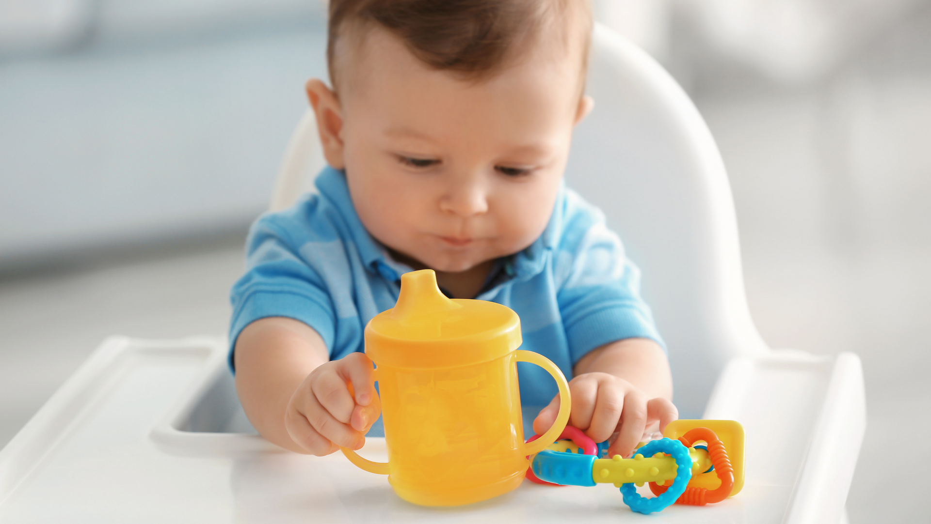 A baby is sitting in a high chair holding a yellow cup and a toy.