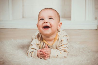 A baby is laying on its stomach on a white rug and smiling.