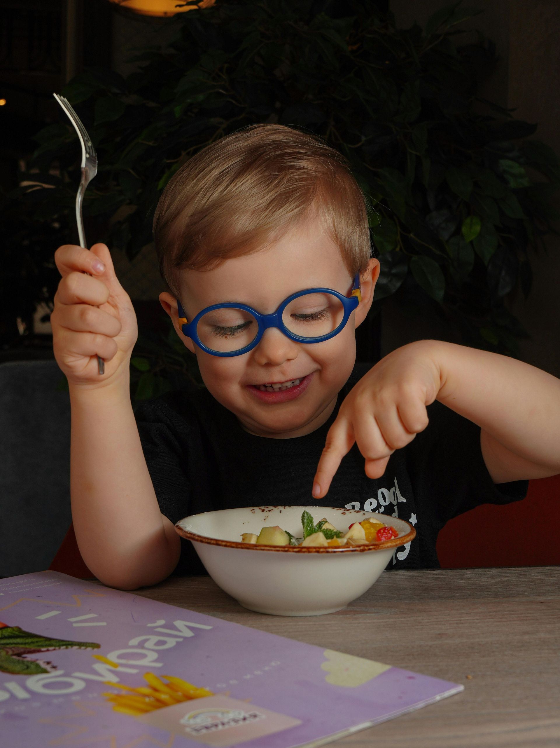 A young boy wearing glasses is eating from a bowl with a fork