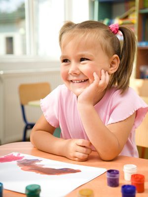 A little girl is sitting at a table with a painting on it.