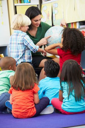 A group of children are sitting on the floor in a classroom looking at a globe.