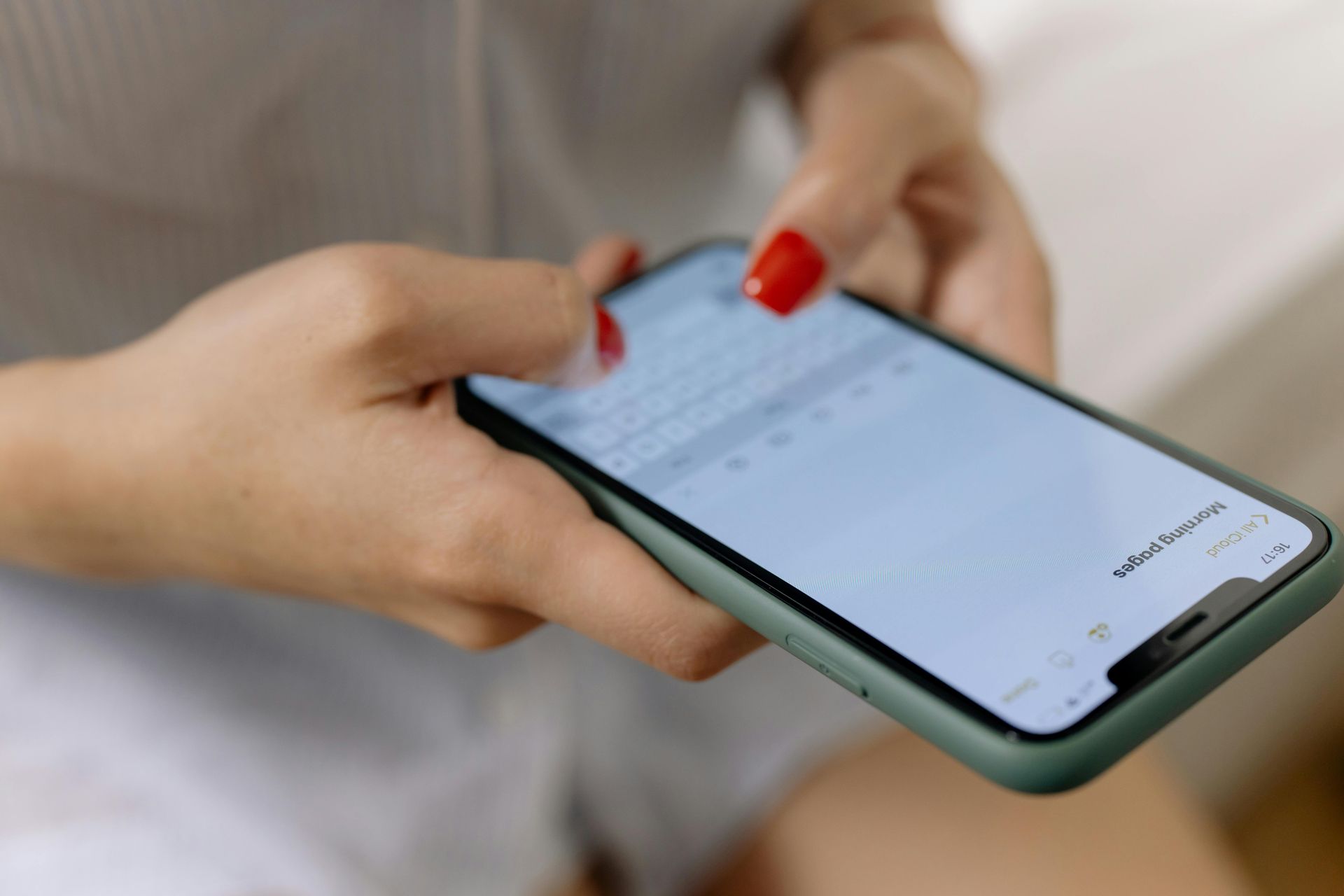 Hands with red nail polish holding a smartphone and tapping its screen