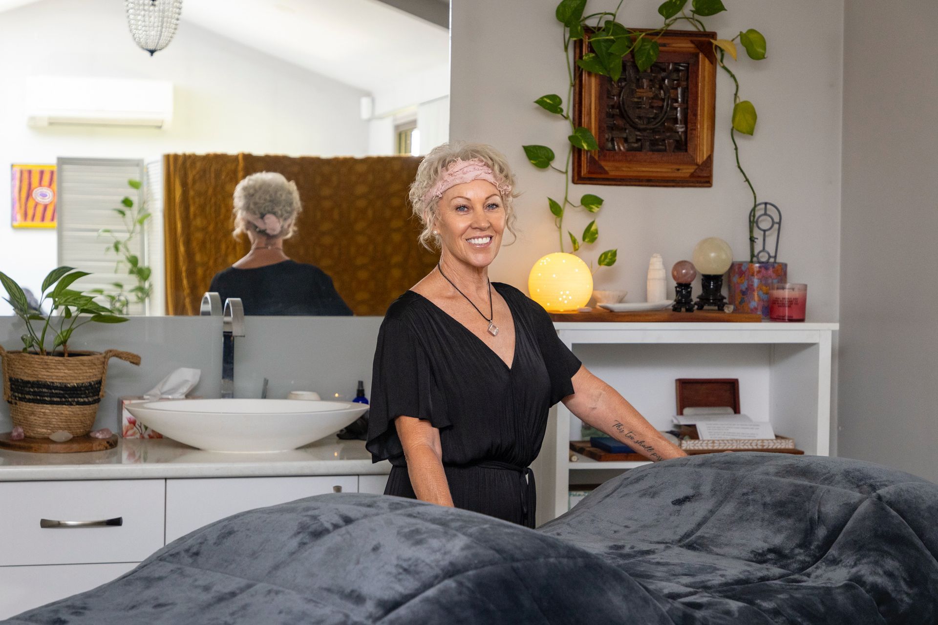 Woman smiling in a bright salon, standing beside a treatment bed with mirrors and plants nearby — Soulfully Happy In Springvale, NSW