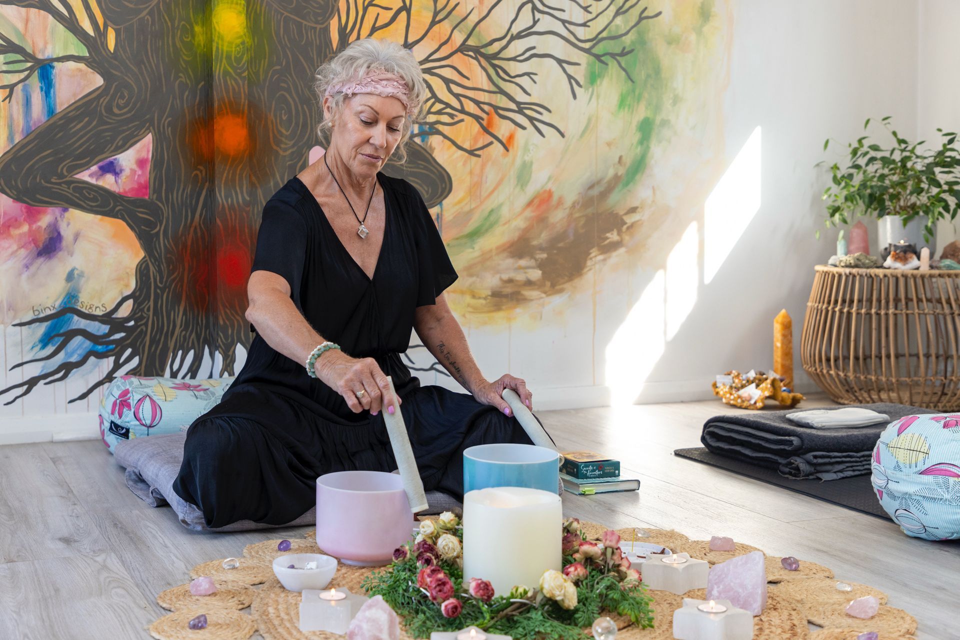 Woman in black seated on a rug, playing a singing bowl among candles and flowers in a serene room — Soulfully Happy In Springvale, NSW