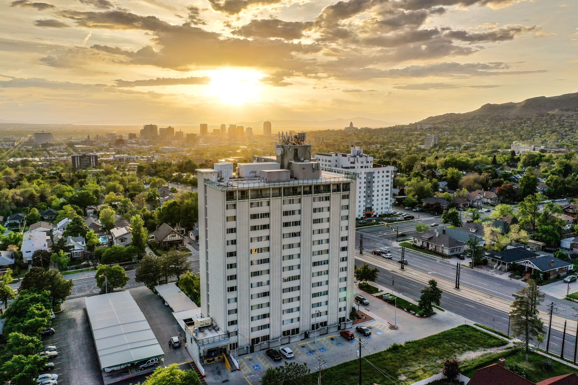 Aerial view of a high-rise building at sunset with a city skyline and green hills in the background