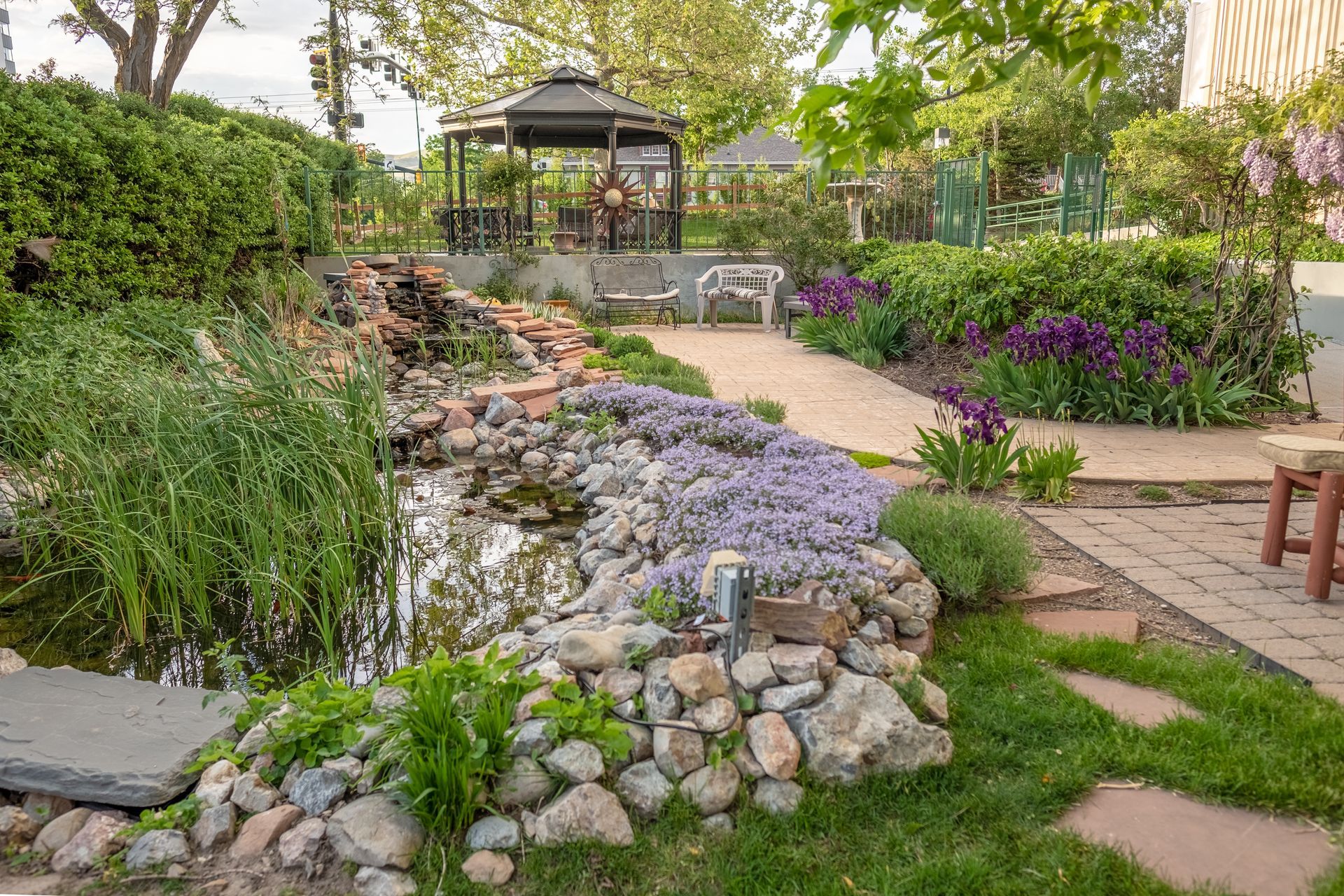 Landscaped garden with a rock waterfall, stone path, and a gazebo under trees