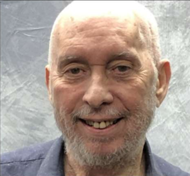 Smiling bald man with a gray beard against a gray backdrop