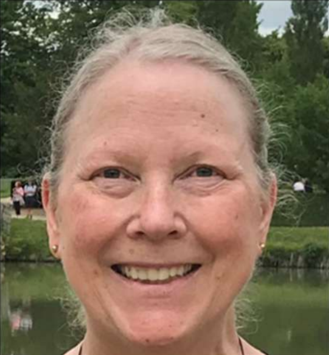Smiling person outdoors by a pond with trees in the background
