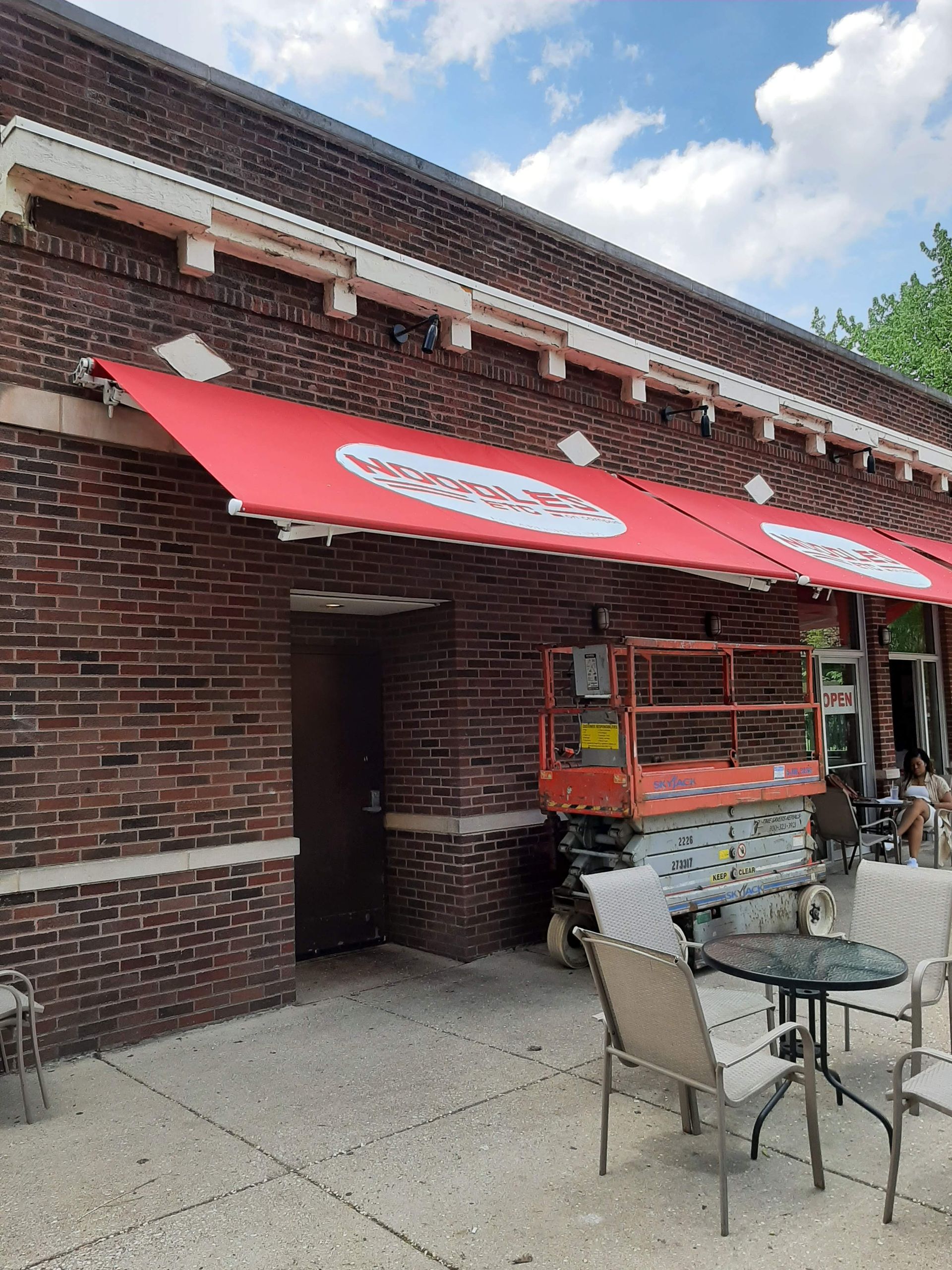A red awning is hanging from the side of a brick building.