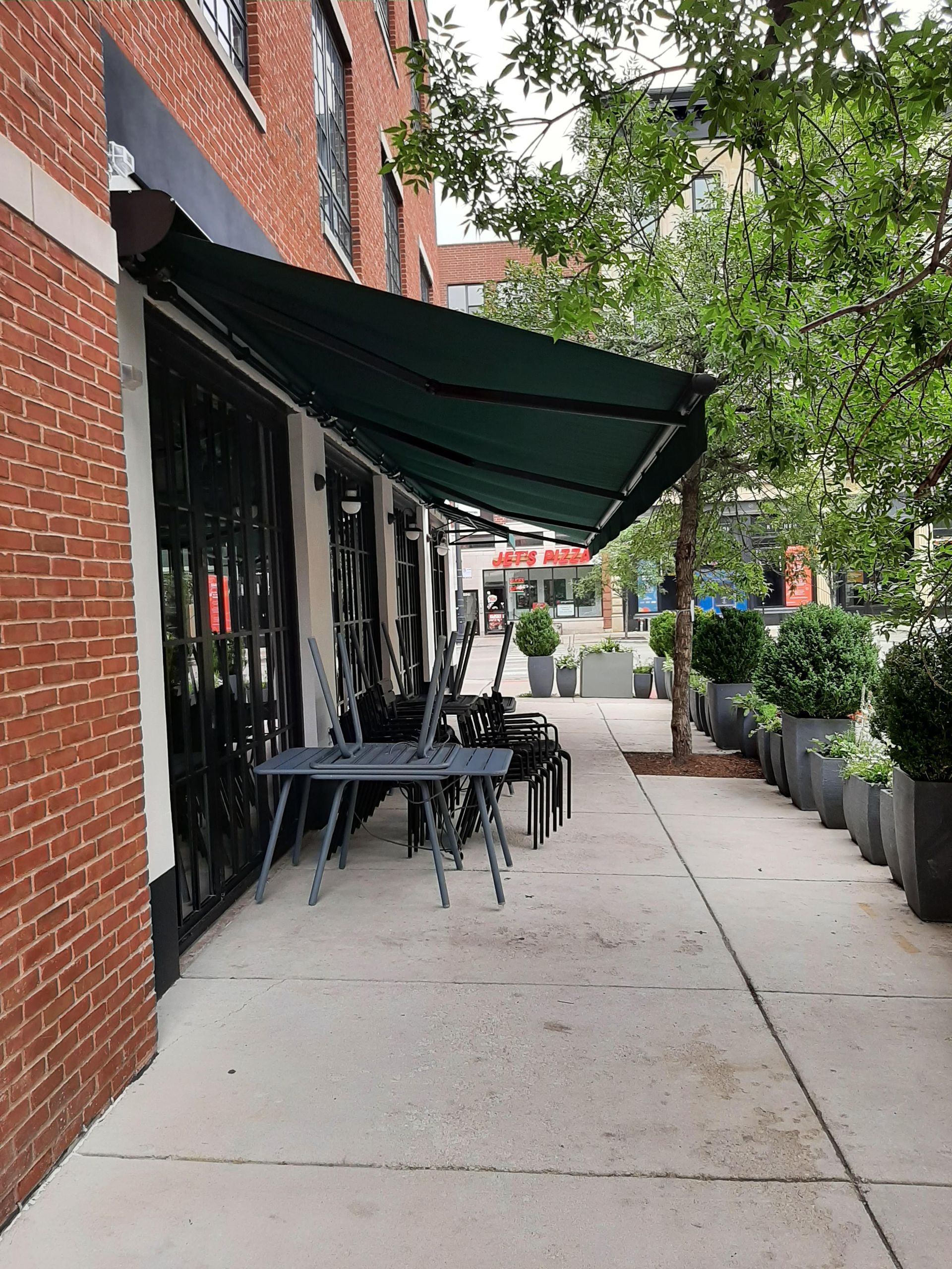 A sidewalk with tables and chairs under an awning