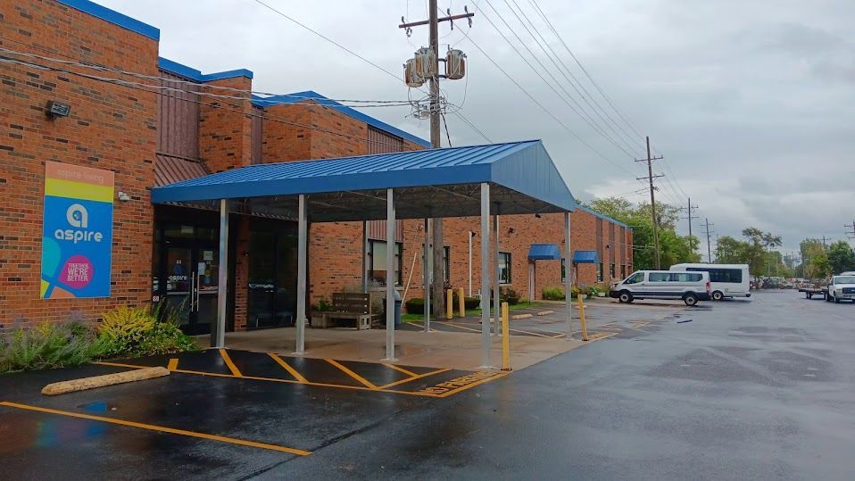 A brick building with a blue awning over the entrance on a rainy day.