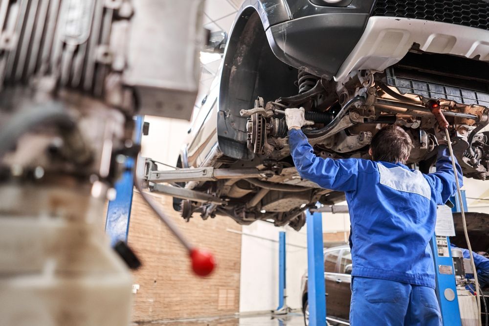 Image of a mechanic assessing and fixing a car that has been lifted.