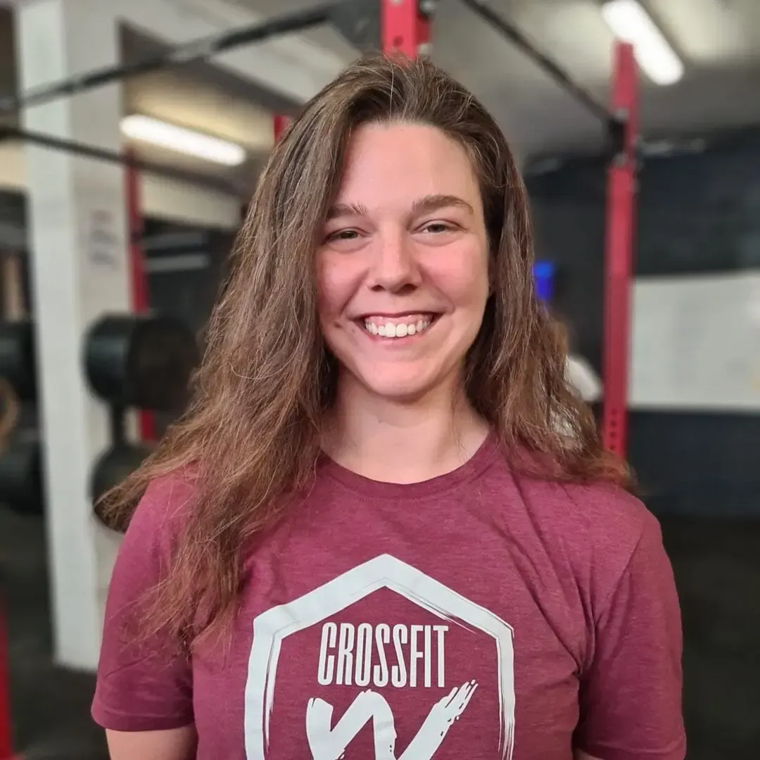 Smiling person in a maroon CrossFit shirt standing in a gym