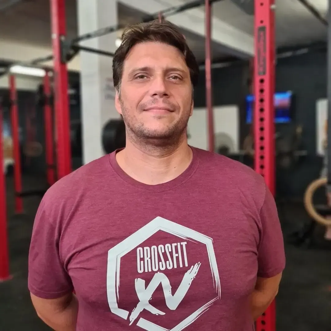 Man standing in a gym, wearing a maroon CrossFit shirt, with red racks in the background