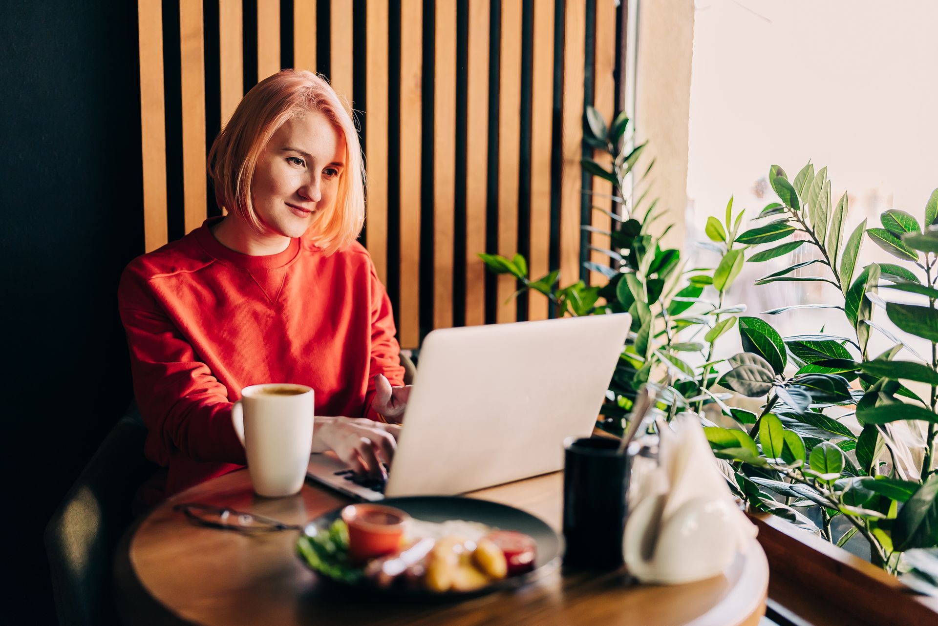A woman is sitting at a table using a laptop computer to add to her blog and generate increased revenue.