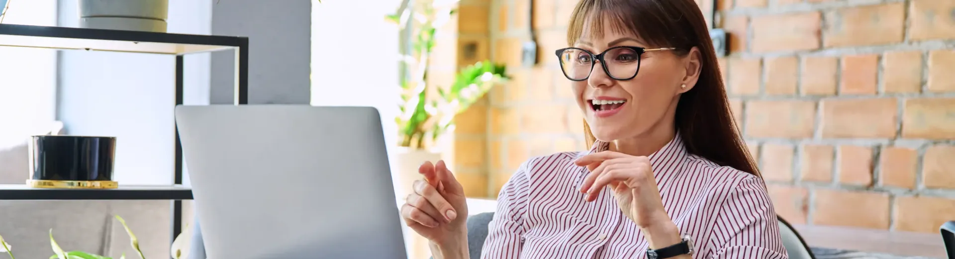 A woman wearing glasses is sitting in front of a laptop computer coaching a client she obtained through her optimized website. 
