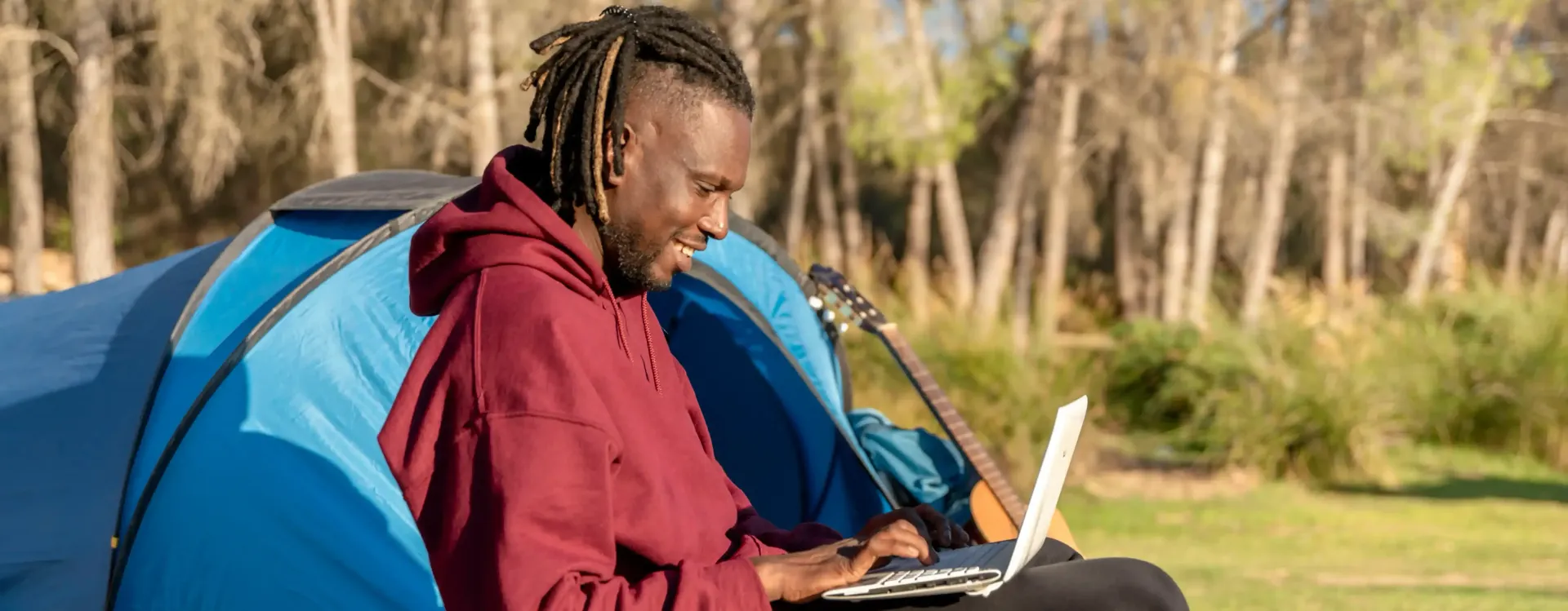 A man is sitting in a tent using a laptop computer.