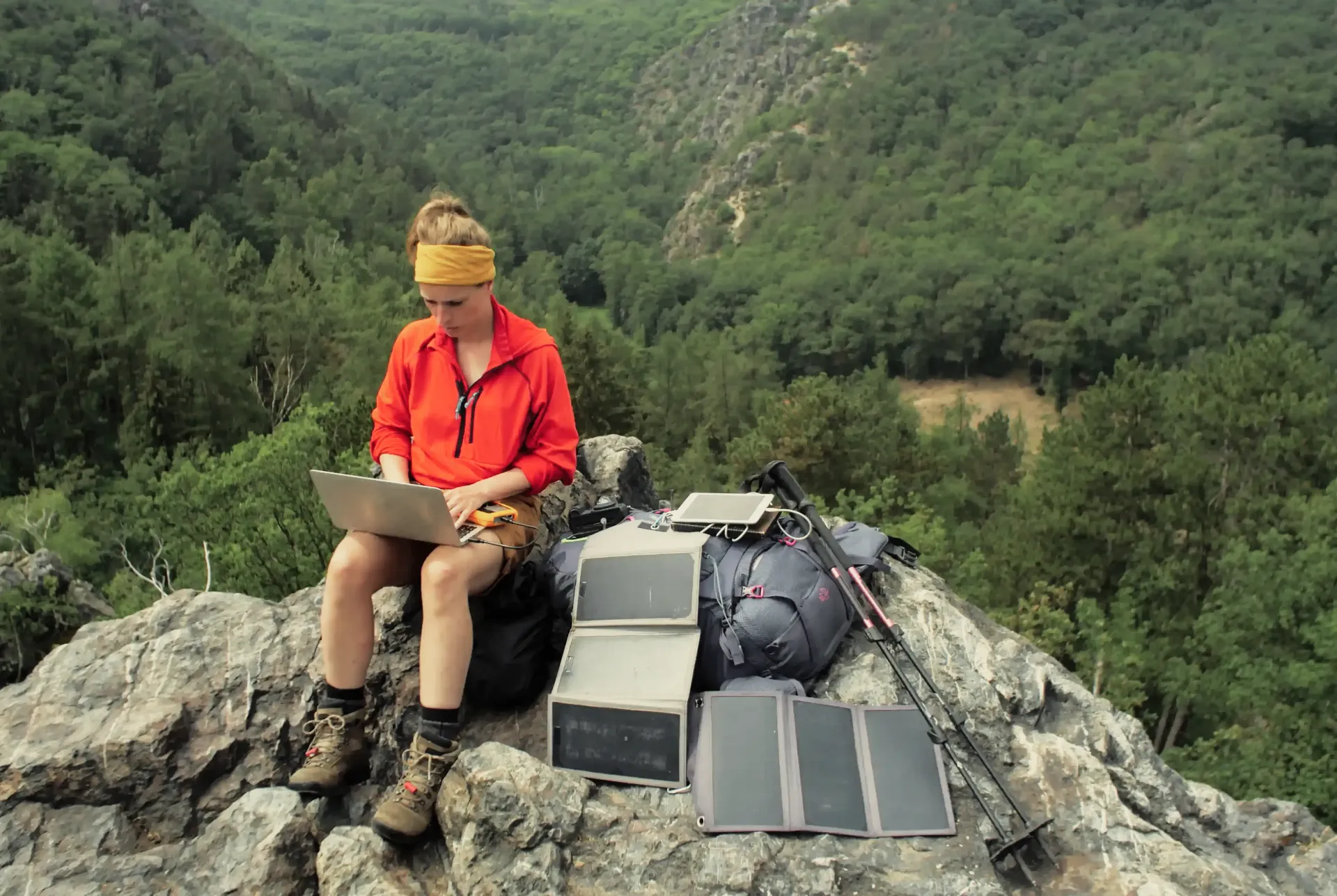 A woman is sitting on a rock using a laptop