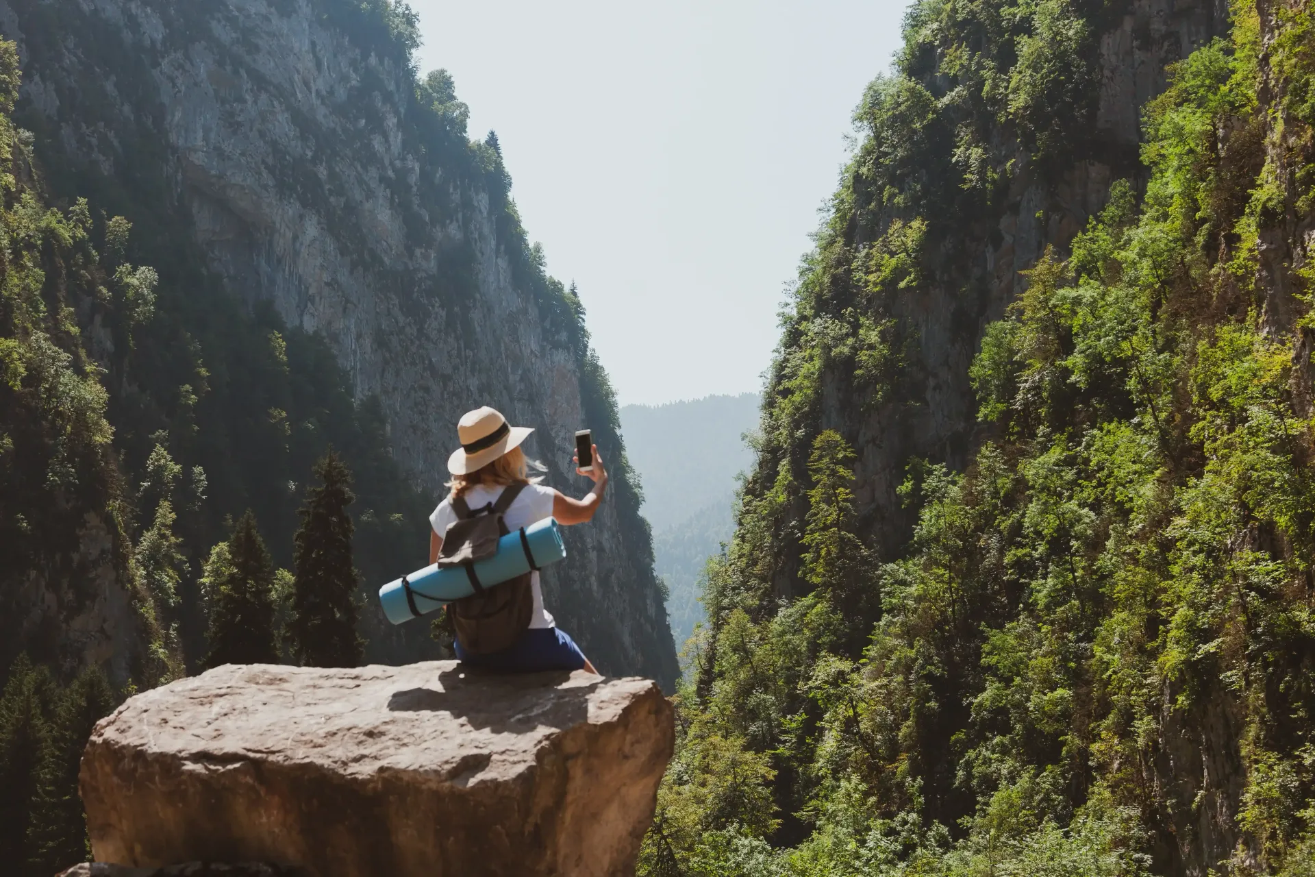 A person is sitting on top of a rock in the mountains taking a selfie.
