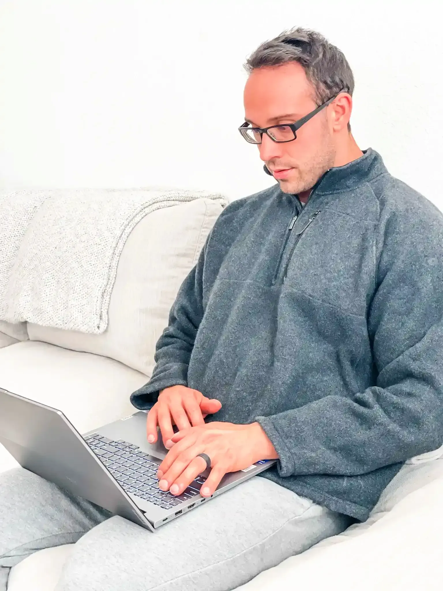 A man is sitting on a couch using a laptop computer.