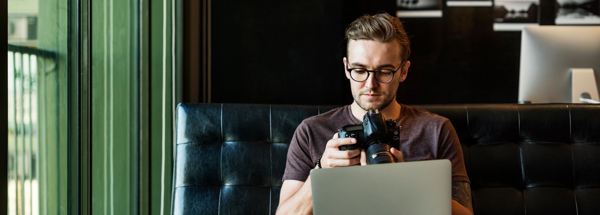 A man is sitting at a table with a laptop and a camera as he adds content to his blog to increase revenue.