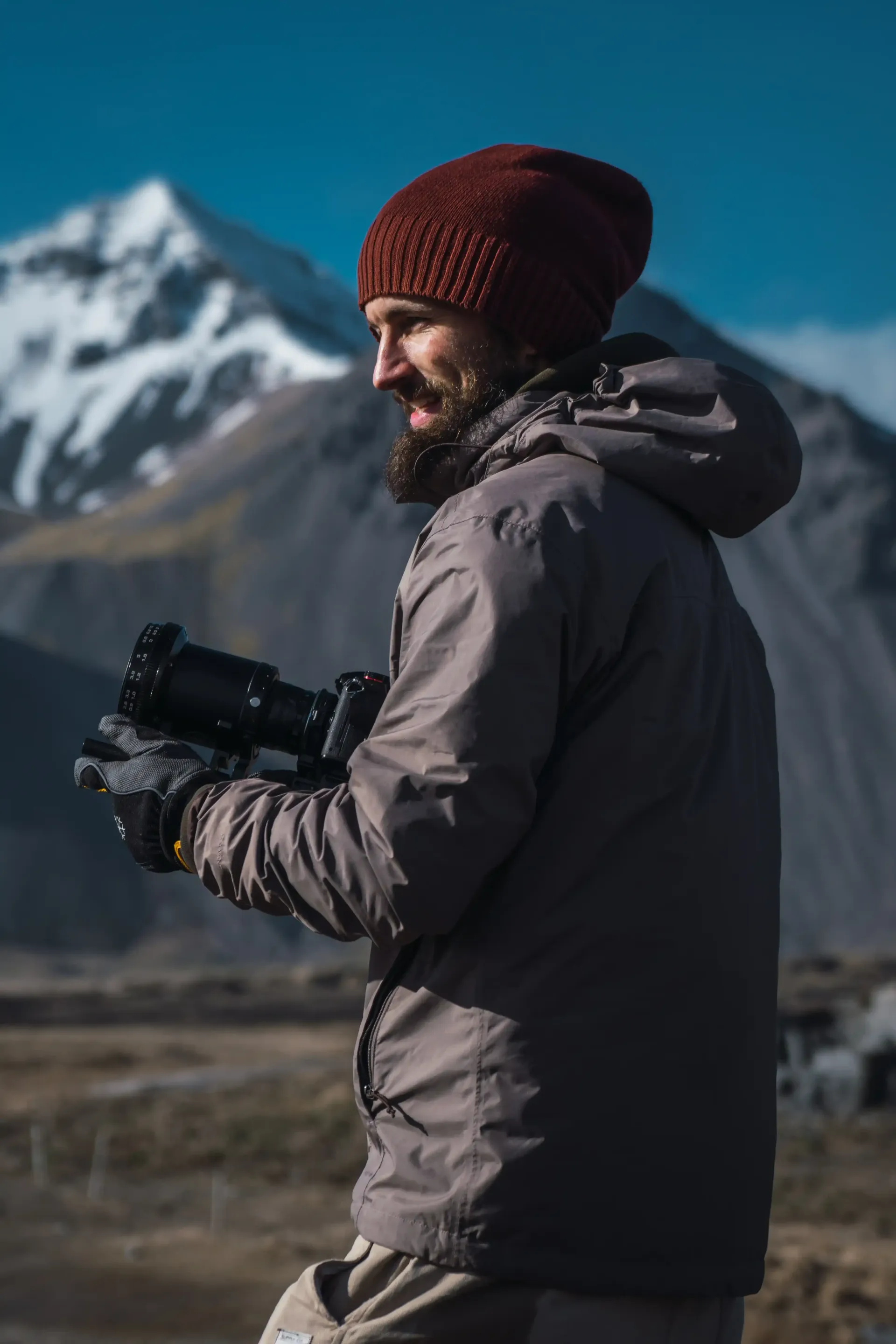 A man with a beard is holding a camera in front of a mountain as he collects content for his SEO optimized website.
