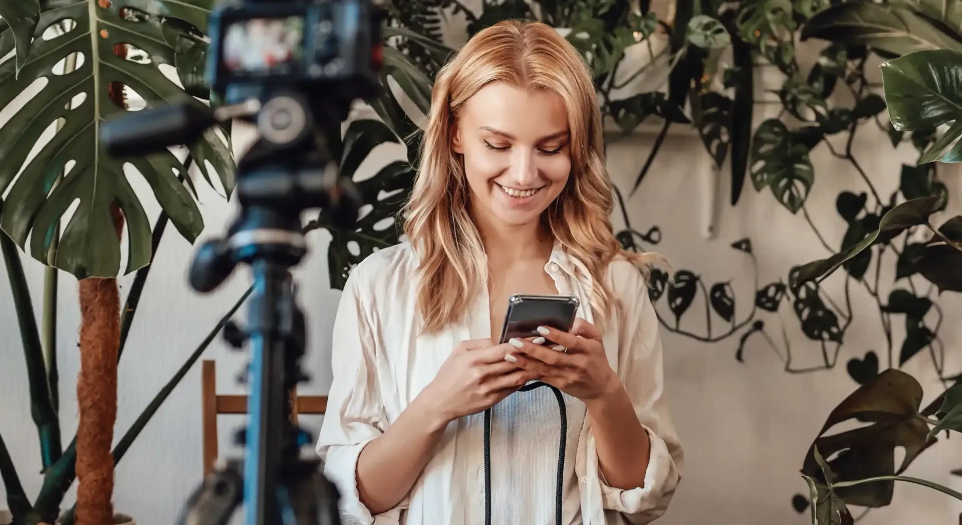 A woman is standing in front of a camera with a phone creating content for her coaching business.
