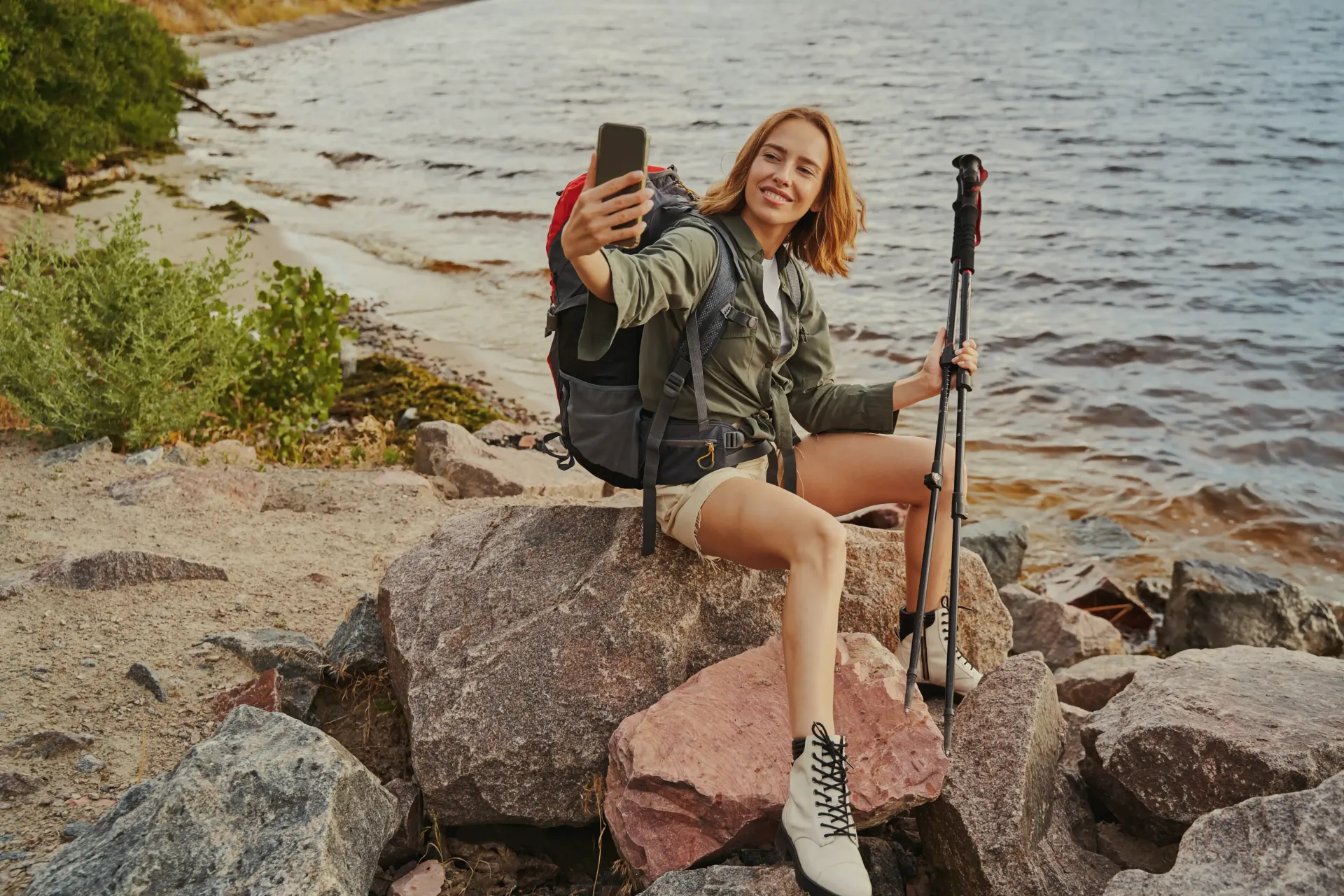 A woman with a backpack is sitting on a rock taking a selfie creating content she can use for her coaching business website that is SEO optimized.