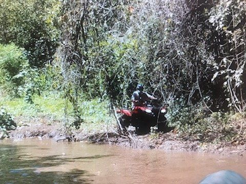 A man is riding a red atv through a muddy river.