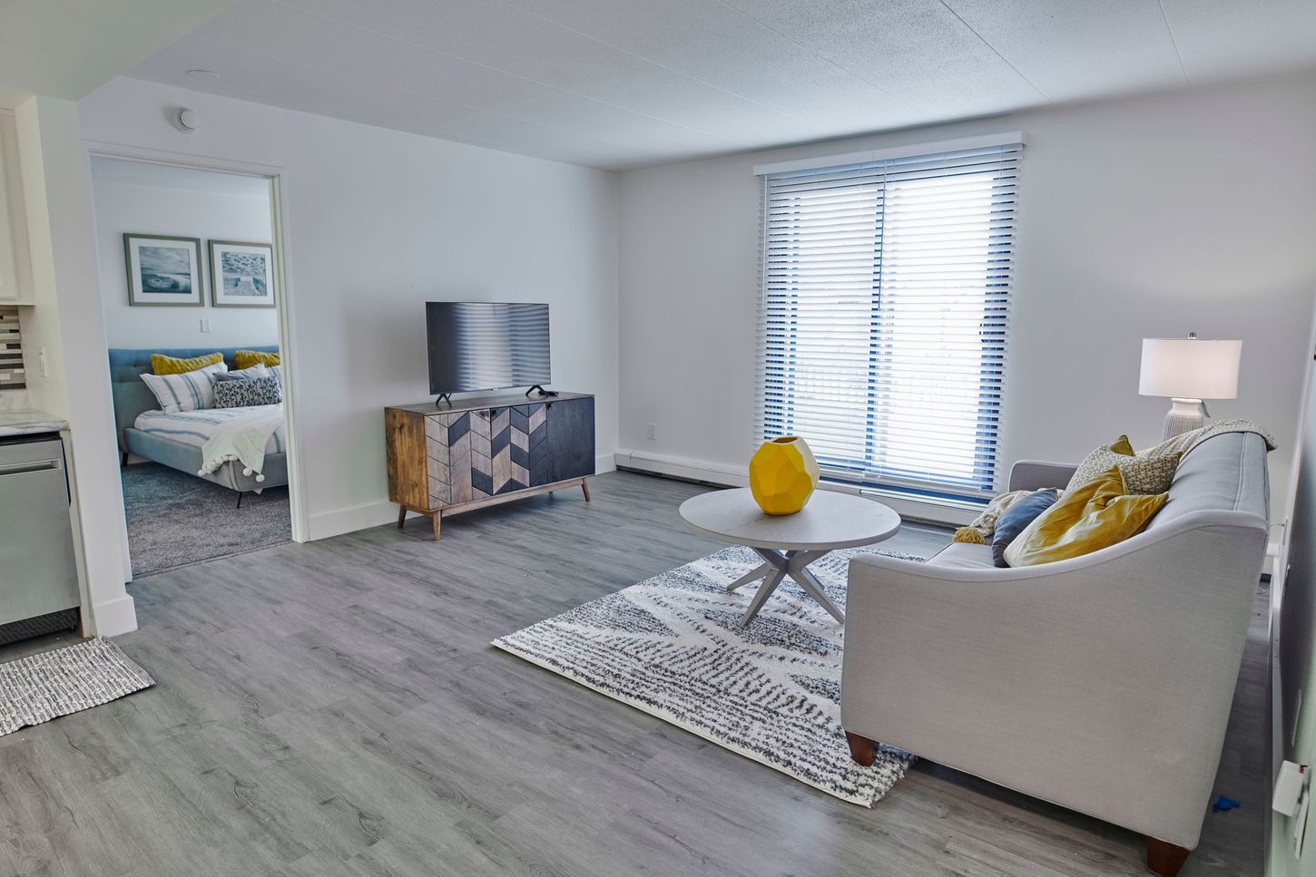 A living room with a couch , coffee table , television and sliding glass doors leading to a bedroom.