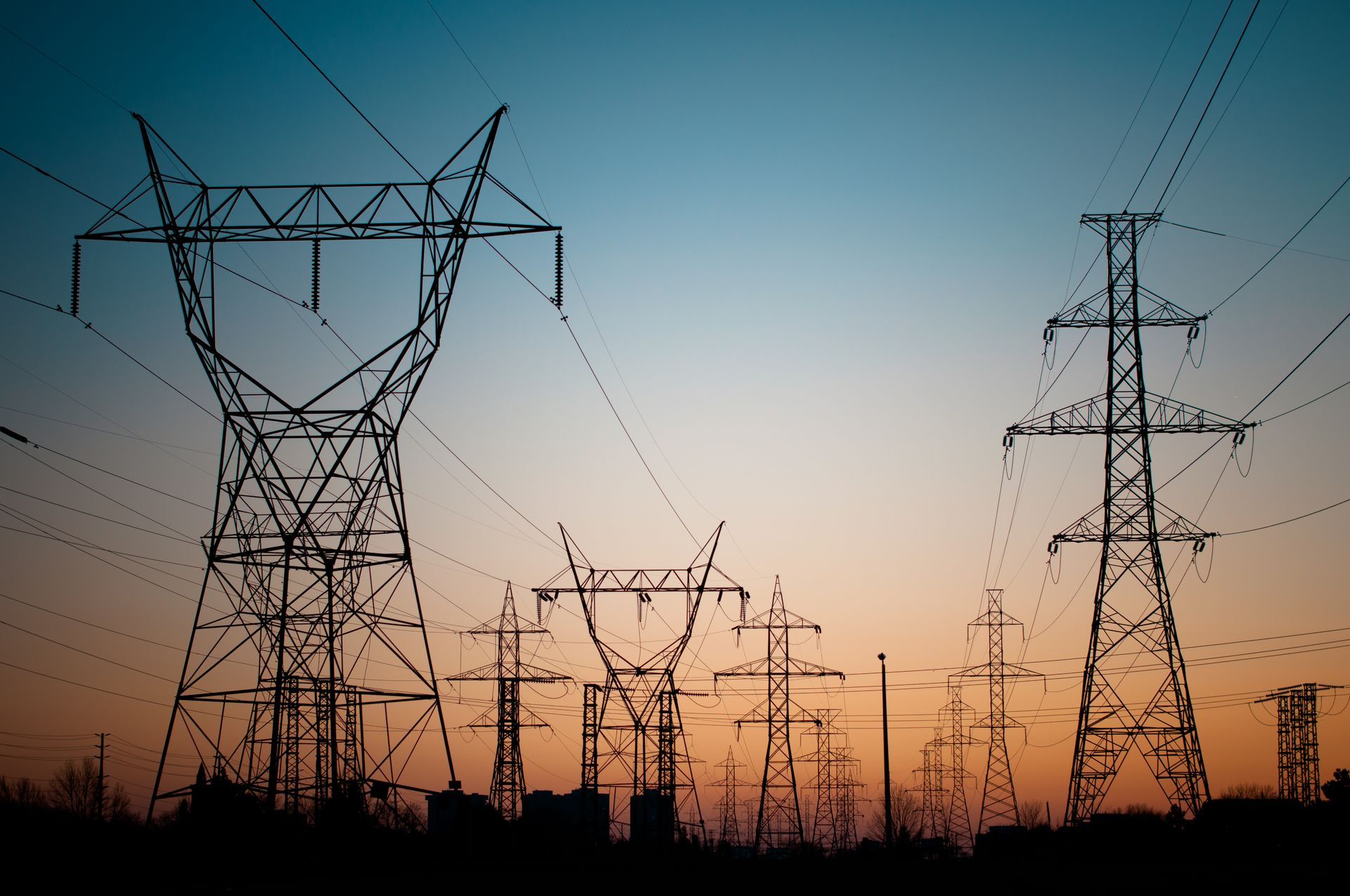A silhouette of numerous high-voltage transmission towers against a gradient sunset sky, representing the vast and complex electricity grid required for New York’s energy distribution.