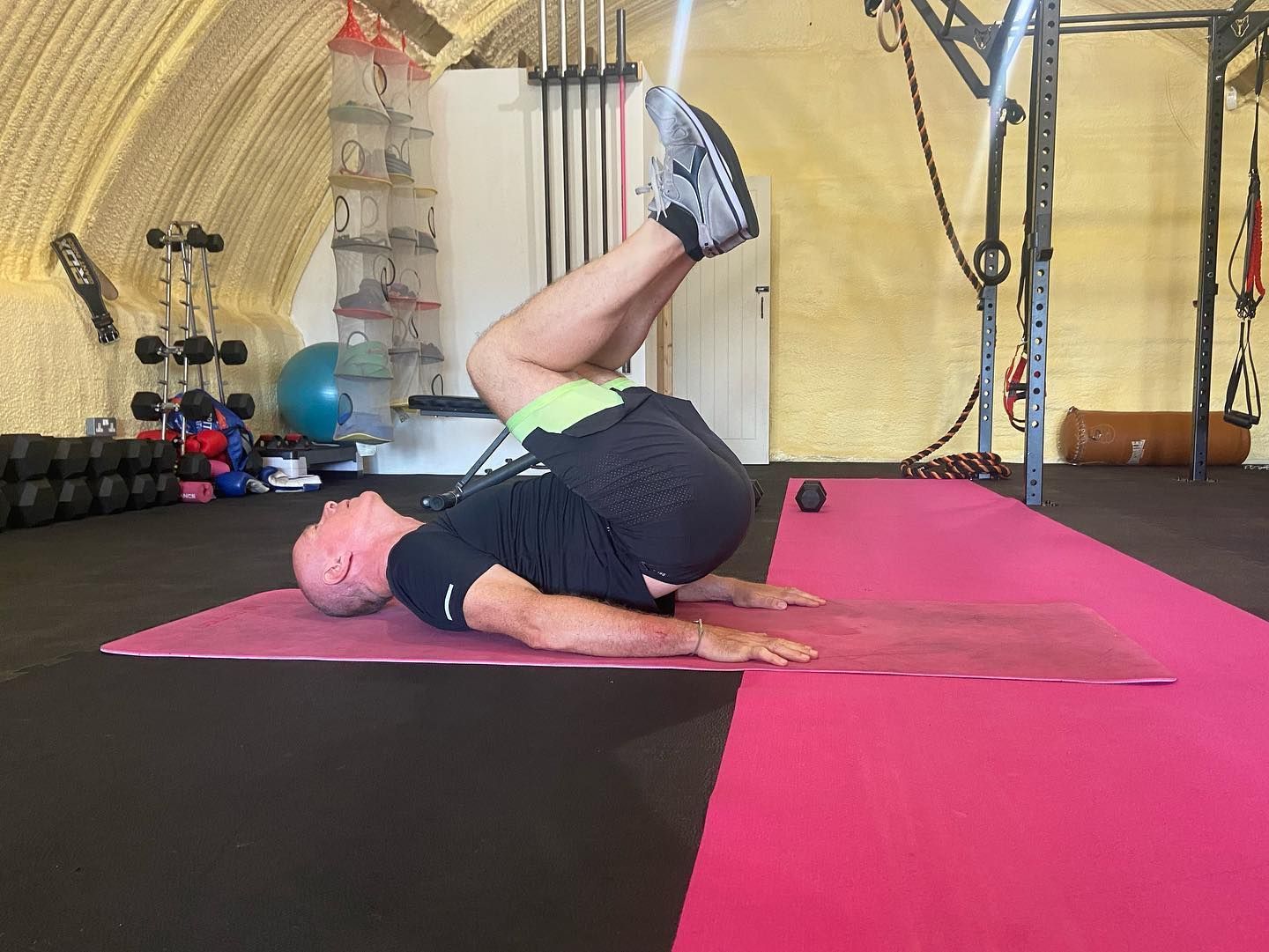 A man is doing a reverse crunch on a pink mat in a gym.