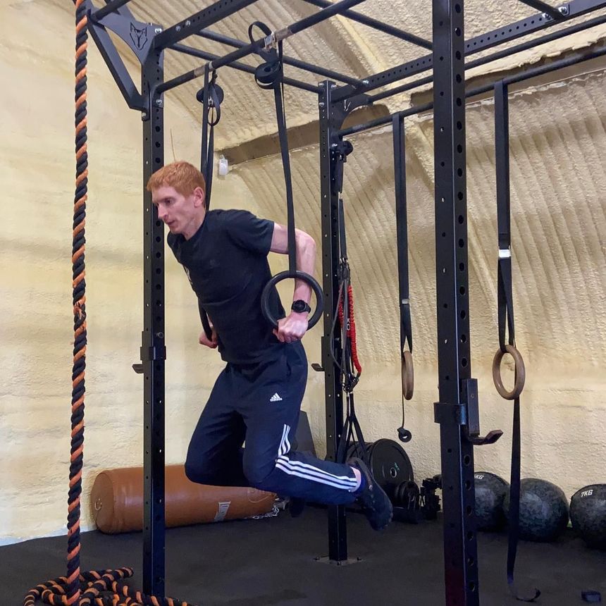 Matt Jolly is doing dips on rings in the JollyFit gym