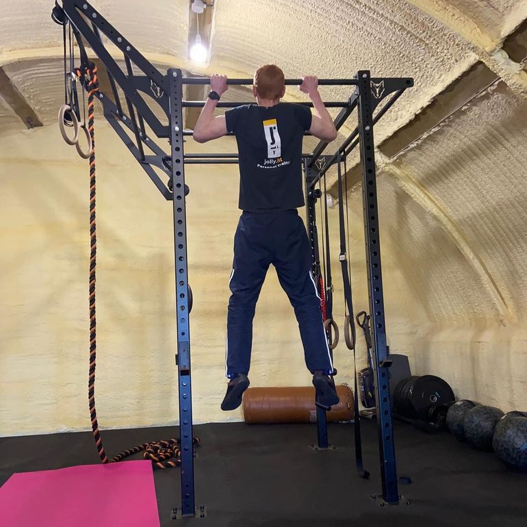 Matt Jolly is doing a pull up in the JollyFit gym