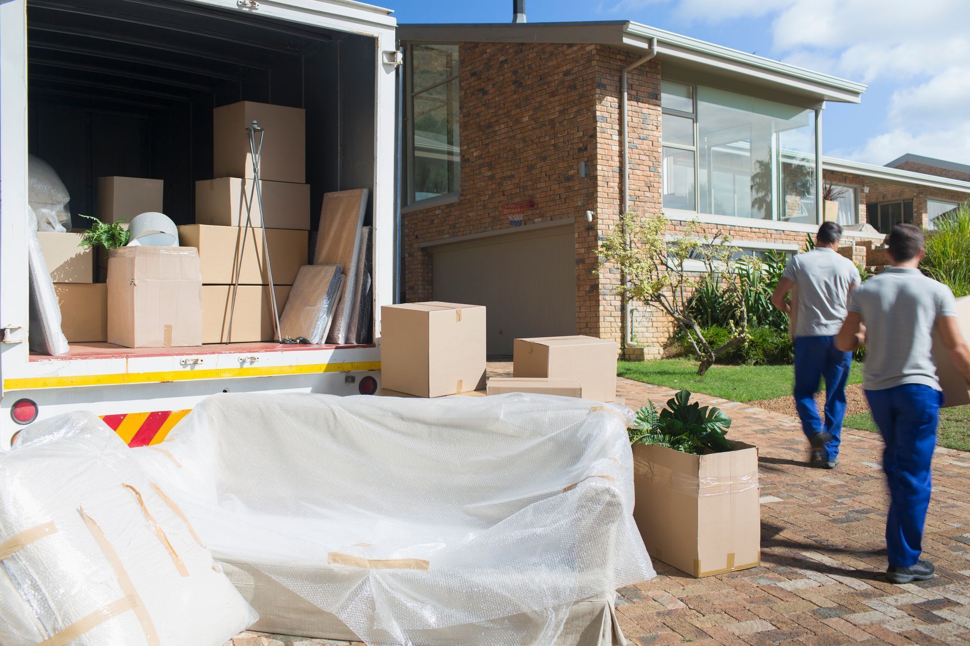 Movers loading a moving truck with boxes and furniture outside a house.