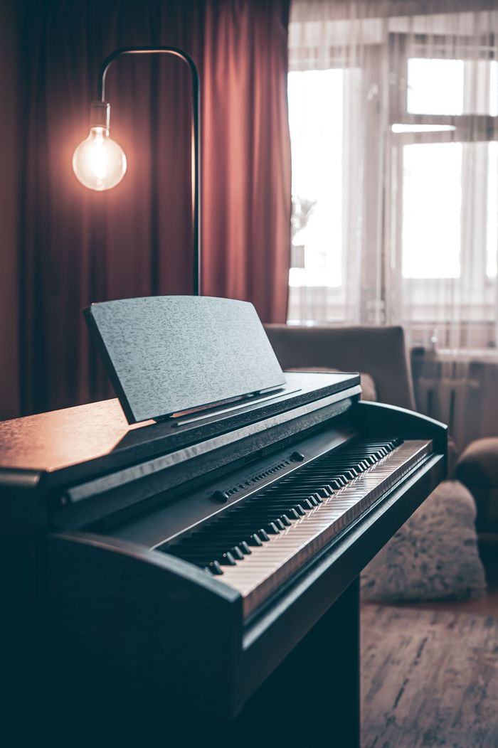 Digital piano with sheet music stand, under a warm light, near a window with curtains.