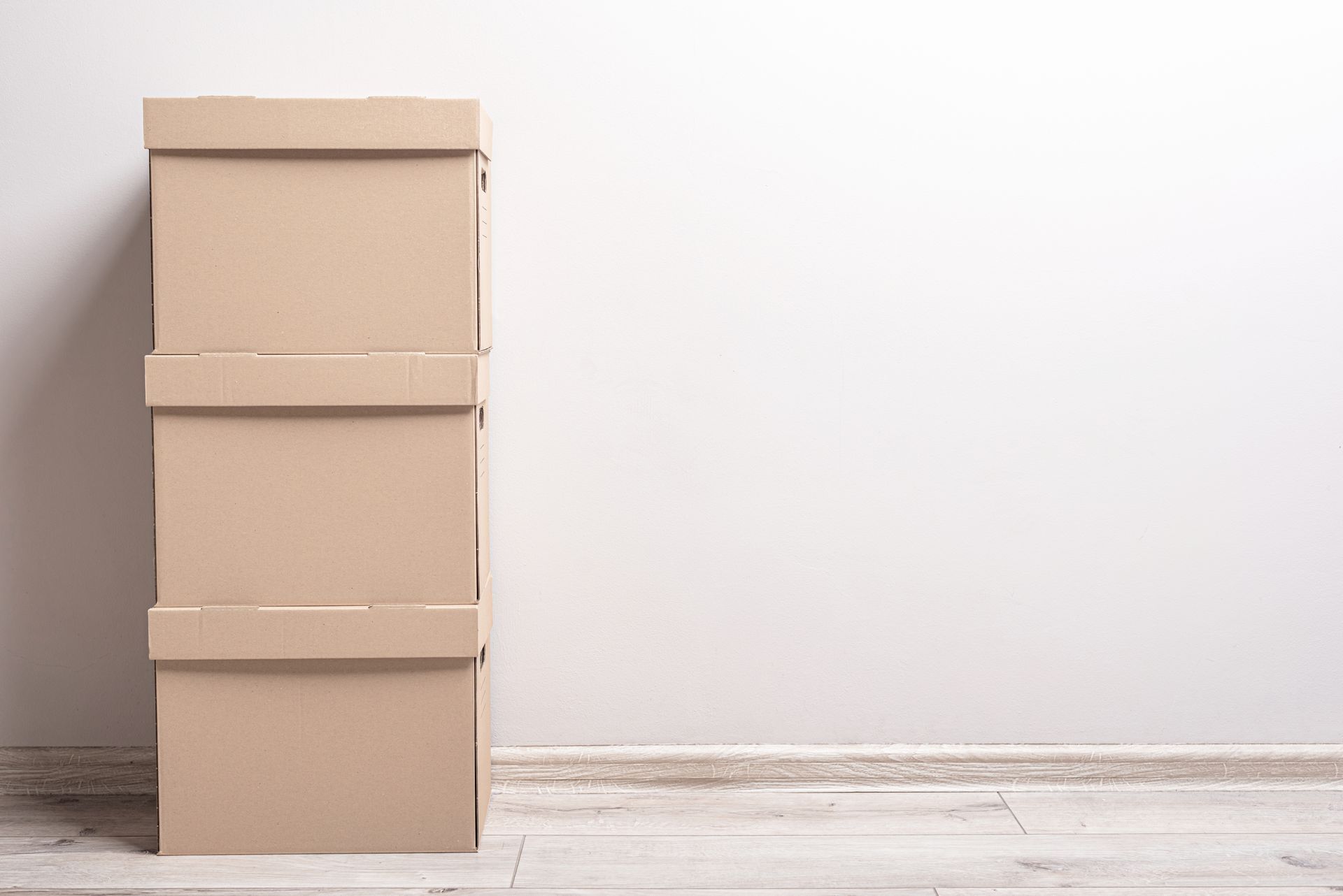 Three stacked cardboard boxes against a white wall and light wood floor.