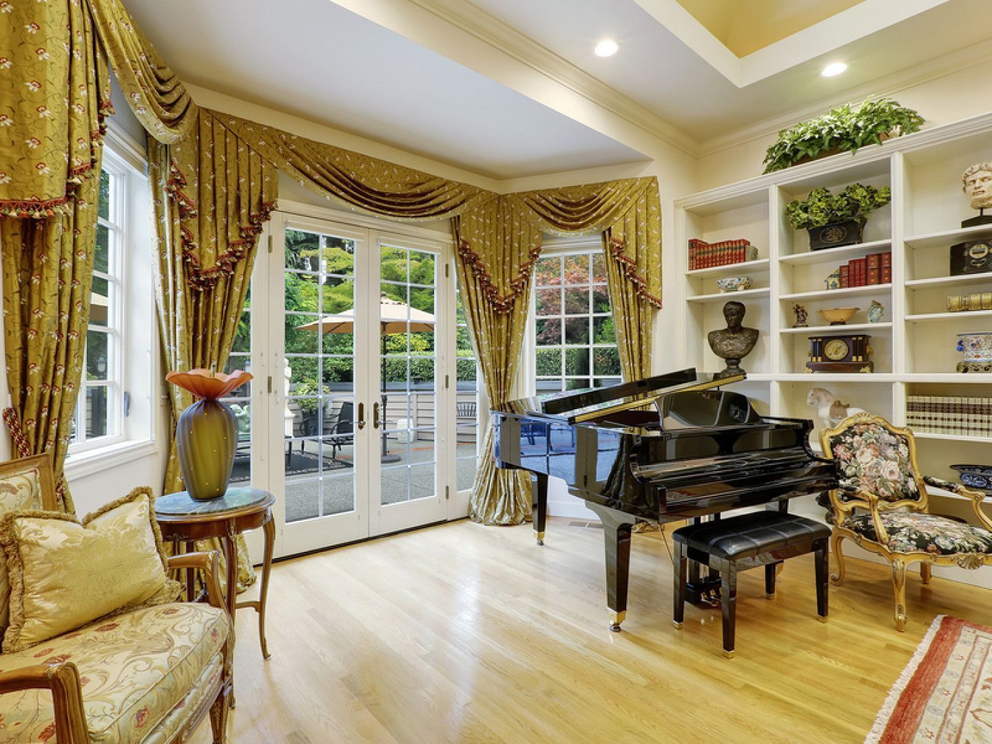 Elegant room with piano, French doors, bookshelves, and ornate gold curtains.