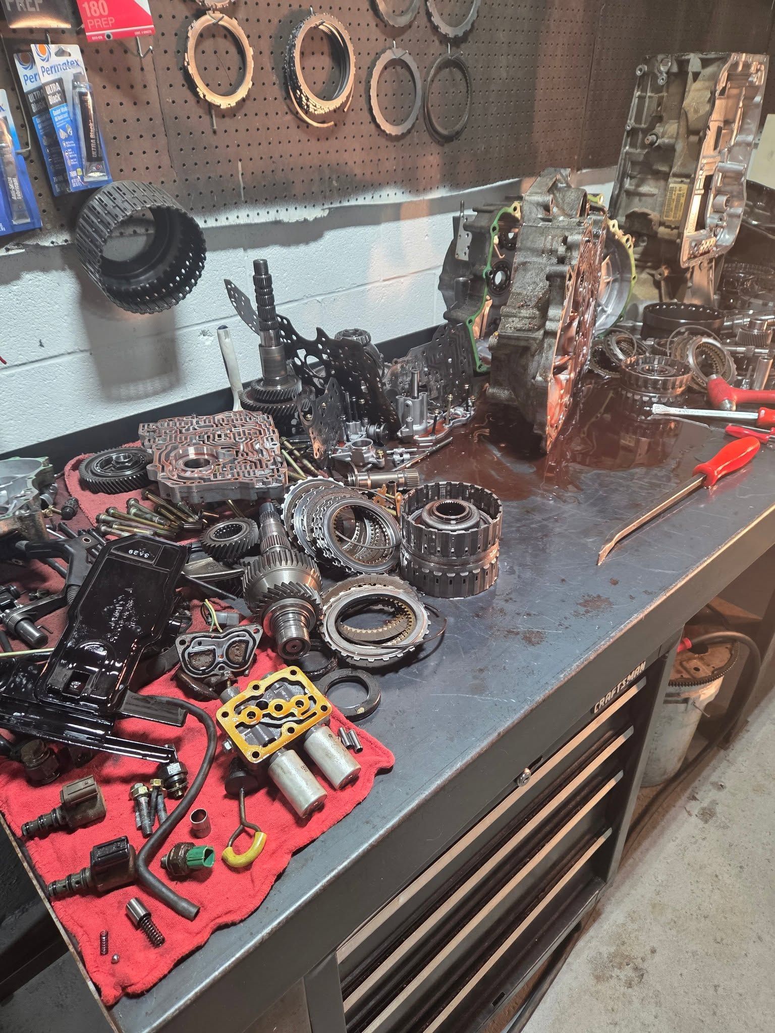 Workbench covered with disassembled engine parts, tools, and red mats in an auto repair shop