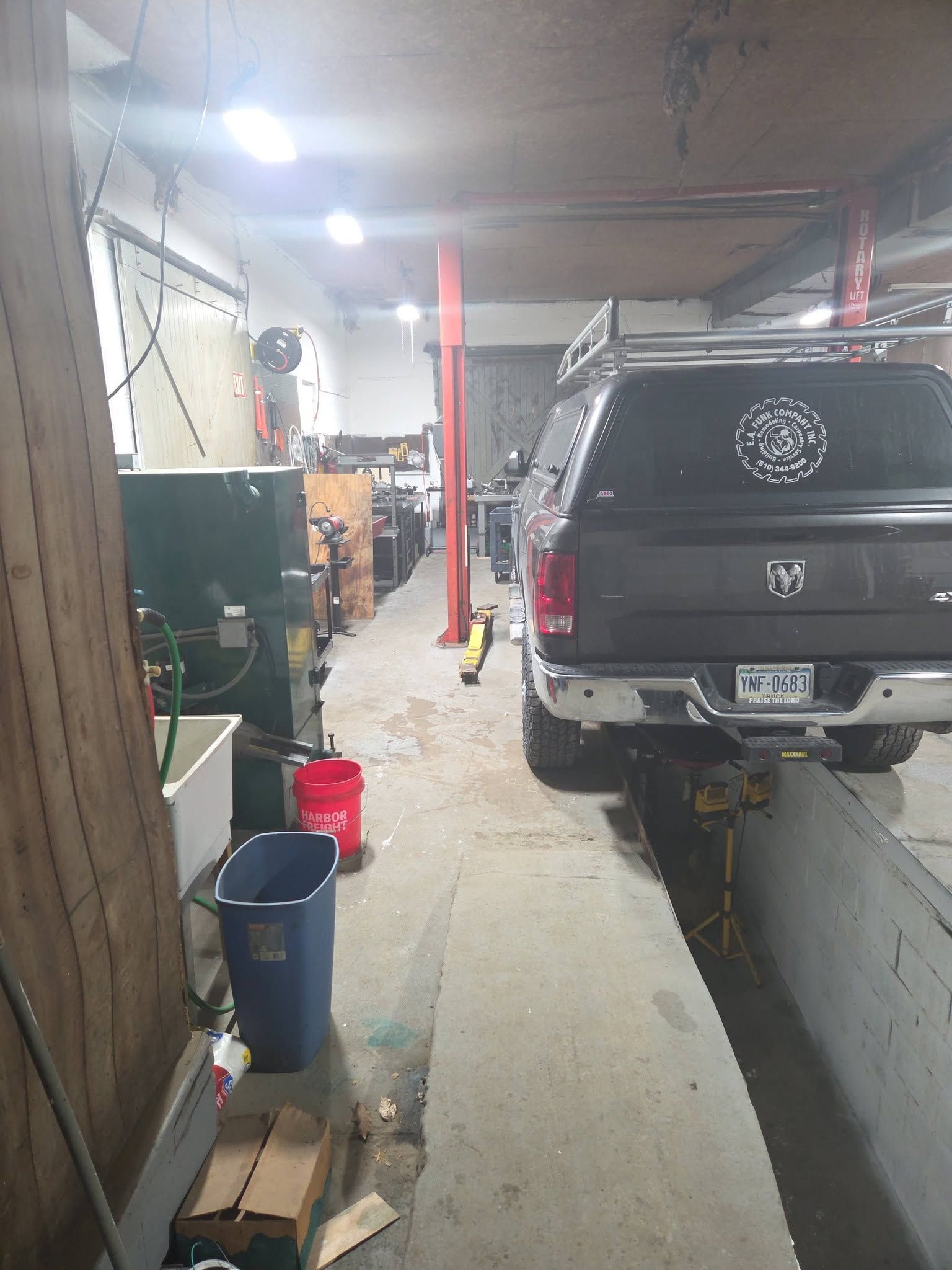 Auto repair garage with a black SUV on a lift beside a narrow work aisle and tools